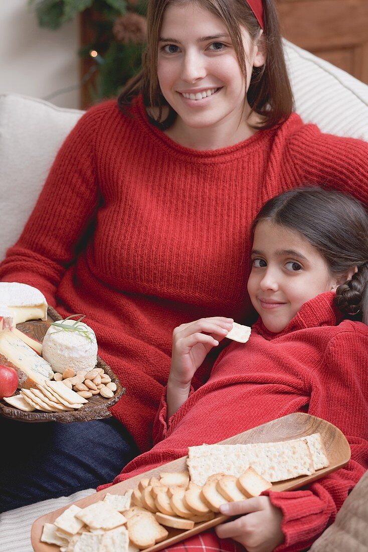 Frau und Mädchen mit Käseplatte und Crackern auf dem Sofa