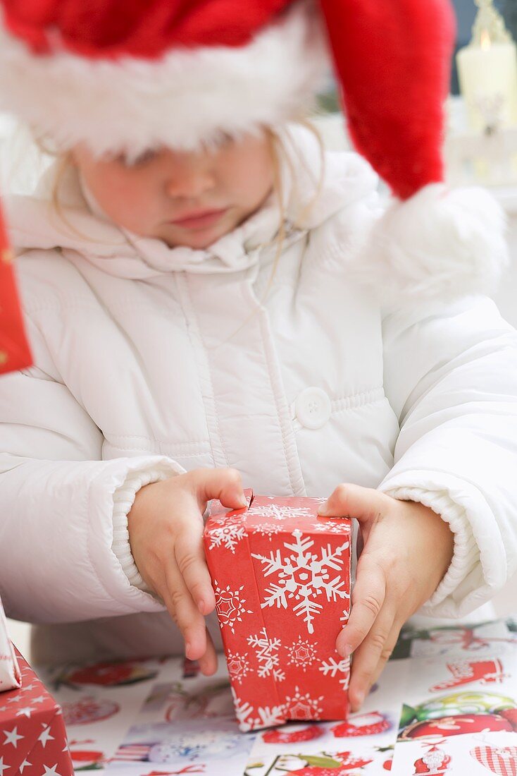 Kleines Mädchen mit Nikolausmütze öffnet Weihnachtspaket