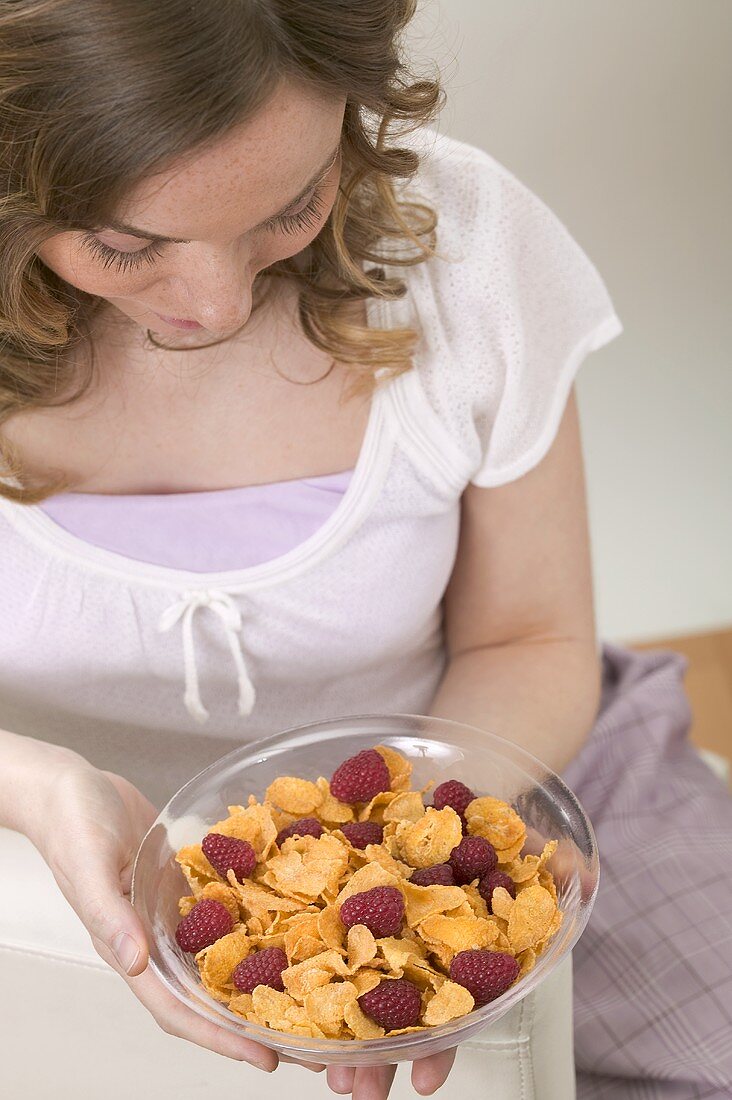 Frau hält Schale Cornflakes mit Himbeeren