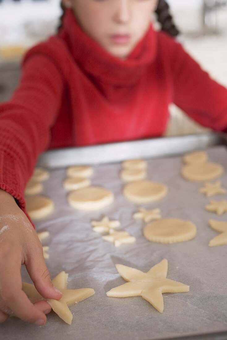 Girl placing cut-out biscuits on baking parchment