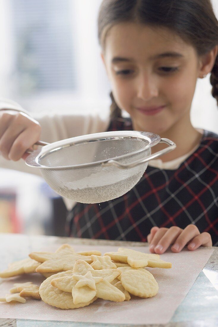 Girl sprinkling biscuits with icing sugar