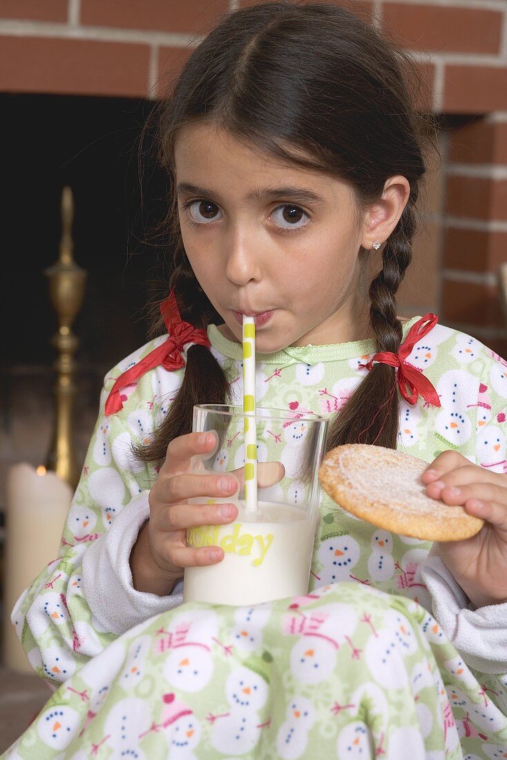 Mädchen trinkt Milch und hält Plätzchen