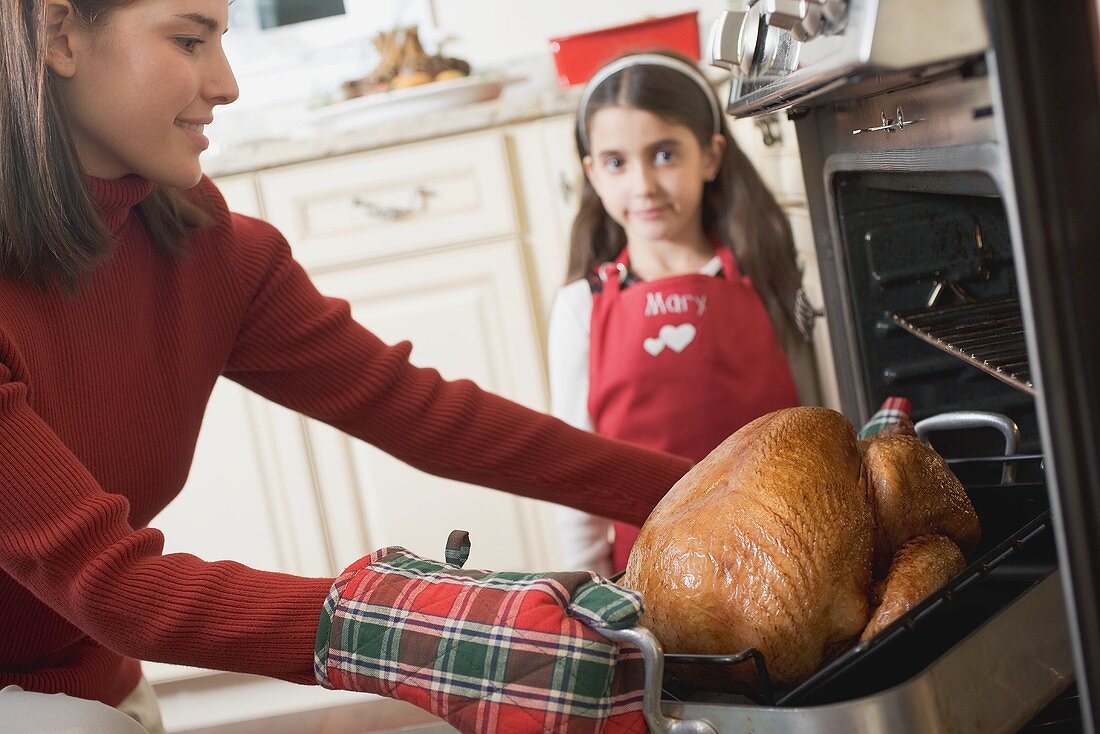 Young woman taking turkey out of oven, girl in background