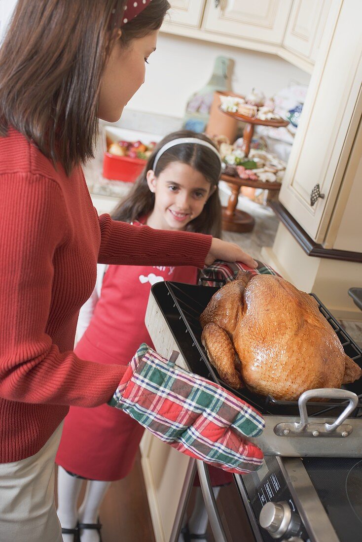 Young woman putting turkey on cooker, girl in background