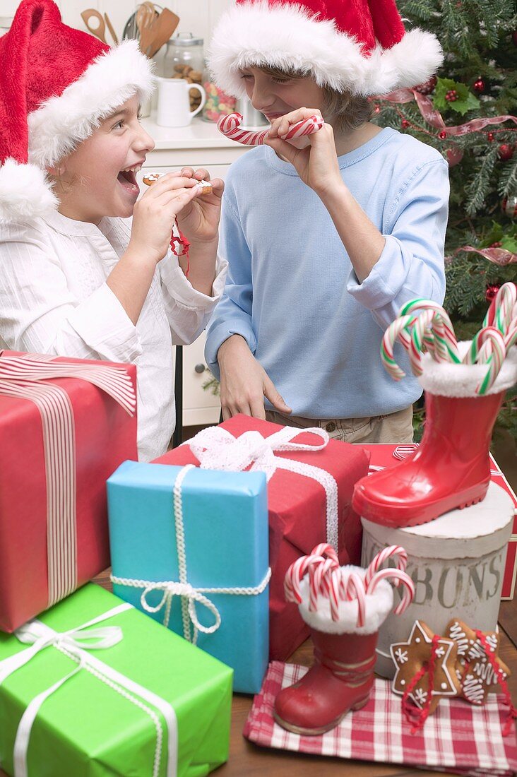 Mädchen und Junge mit Weihnachtsmützen und Geschenken
