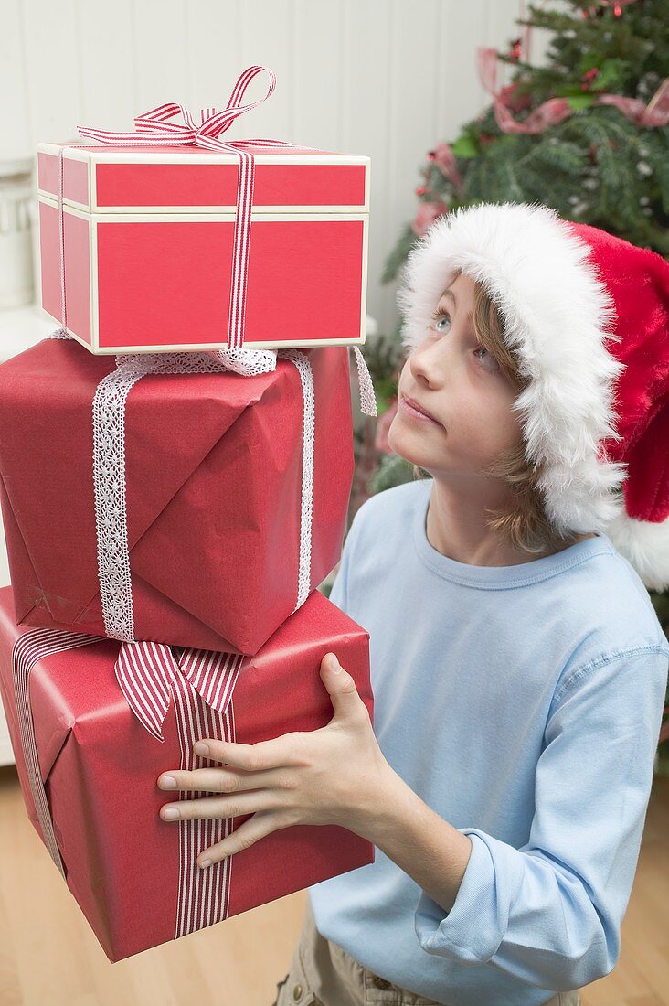 Boy in Father Christmas hat carrying pile of parcels