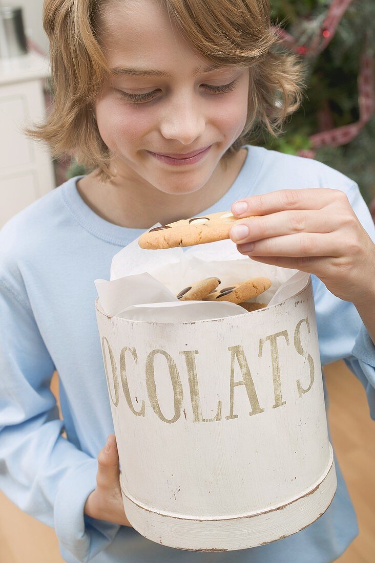 Boy taking chocolate chip cookie out of cookie tin