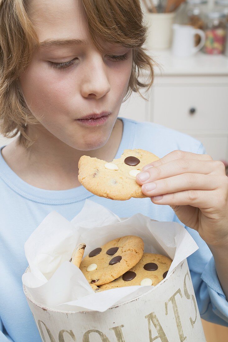 Boy eating chocolate chip cookie out of cookie tin