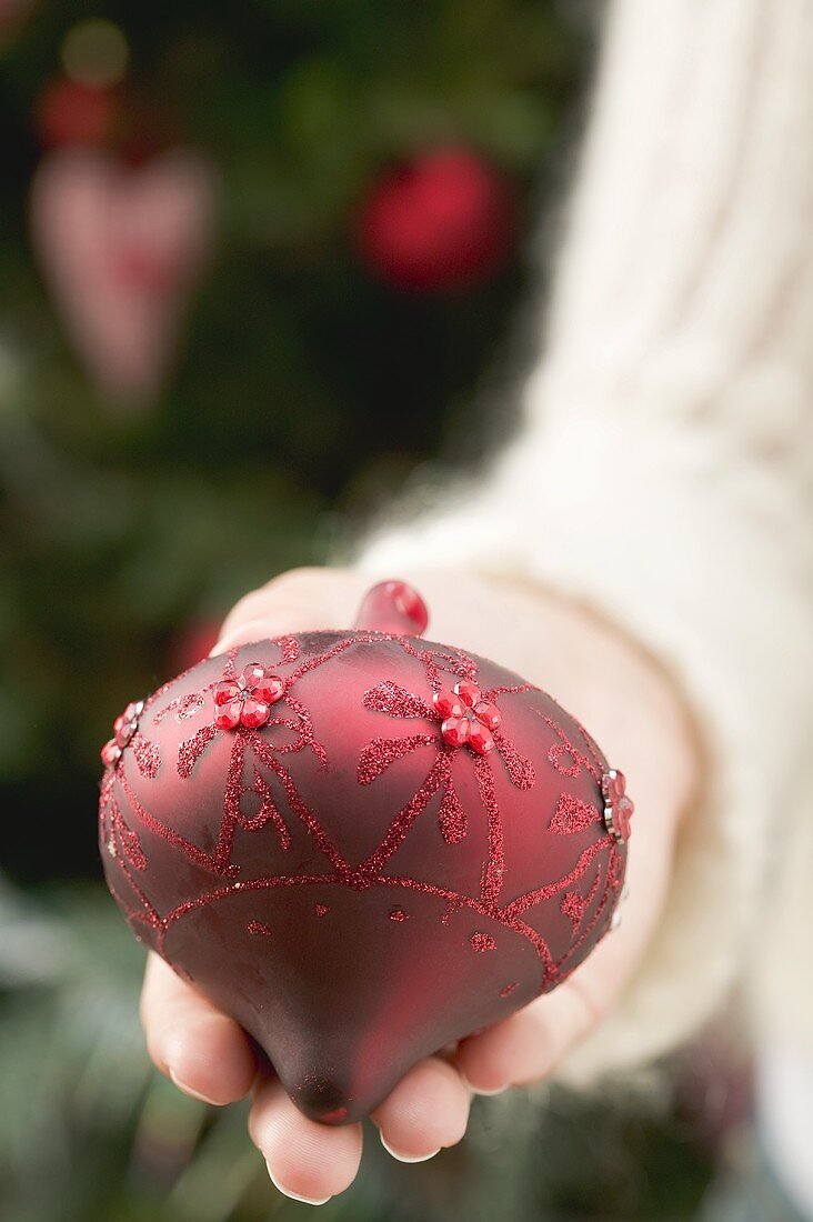 Hand hält rote Christbaumkugel