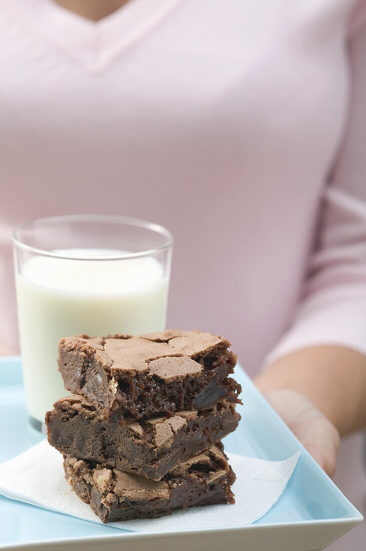 Frau hält Brownies und Glas Milch auf quadratischem Telller