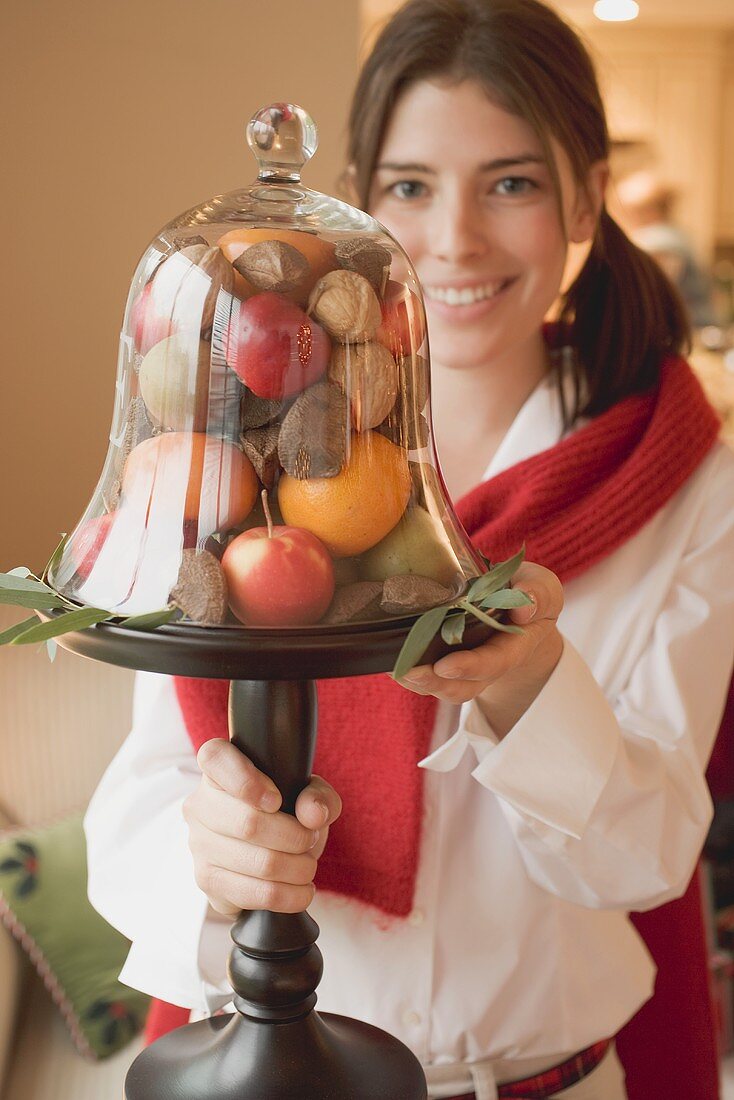Woman holding fruit under glass cover (Christmas table decoration)