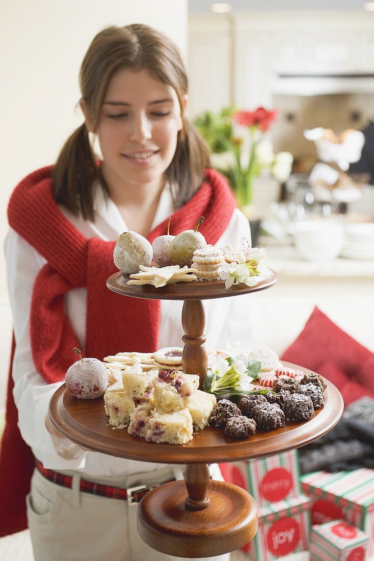Young woman holding tiered stand full of Christmas fancies