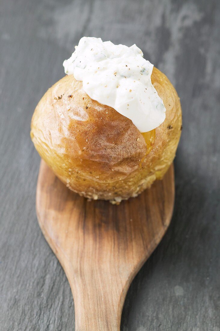 Baked potato with quark on wooden spoon