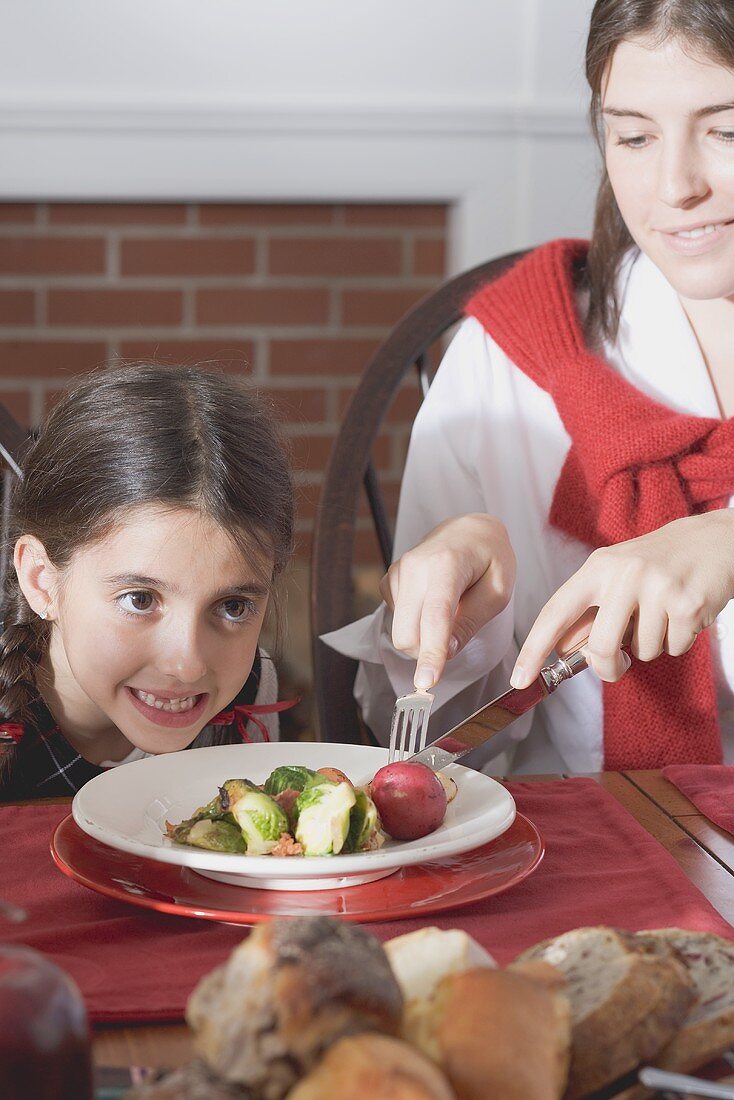 Junge Frau zerteilt für kleines Mädchen Gemüse am Teller