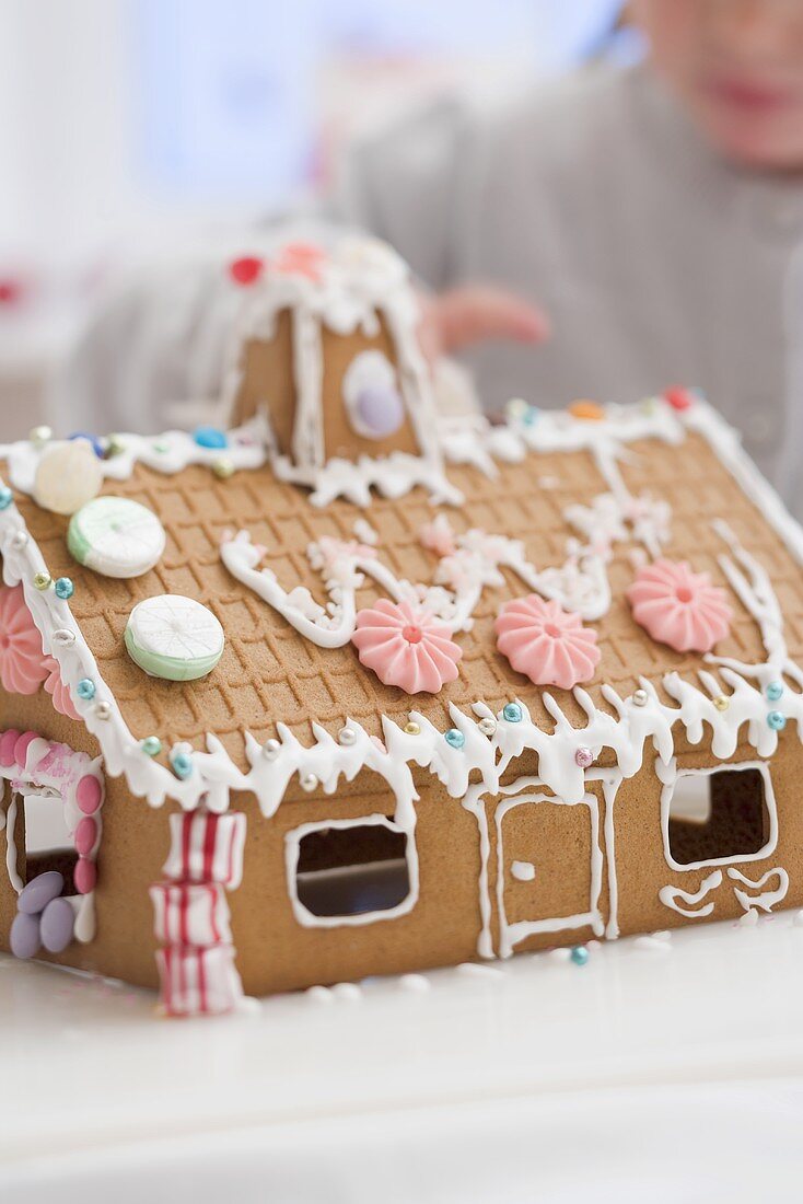 Kind verziert Lebkuchenhaus mit Zuckerperlen