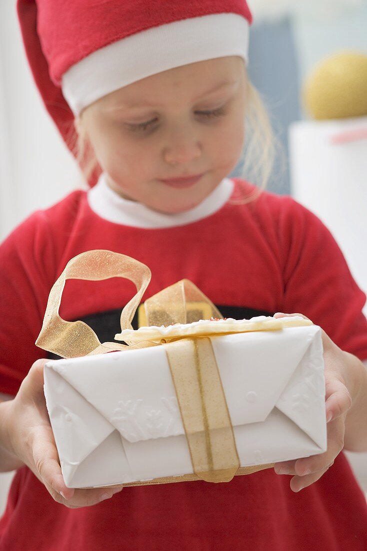 Kleines Mädchen im Weihnachtsmannkostüm hält Geschenk