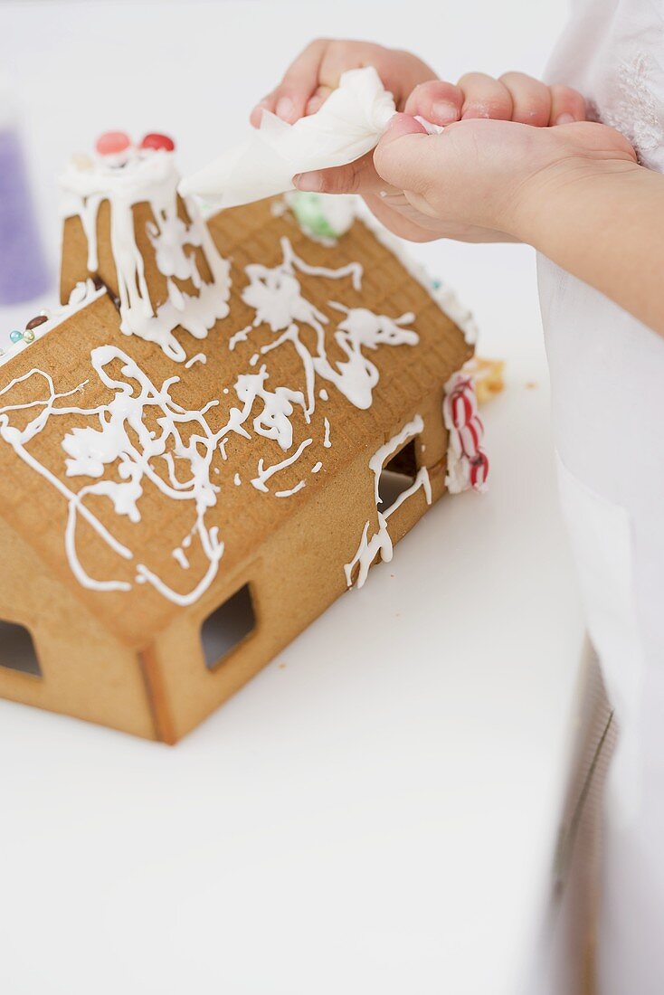 Kind verziert Lebkuchenhaus mit Spritztüte
