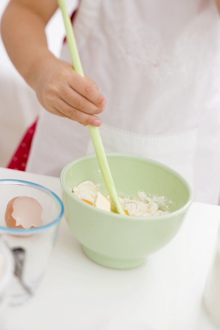 Kleines Mädchen verrührt Ei, Mehl und Butter mit Kochlöffel