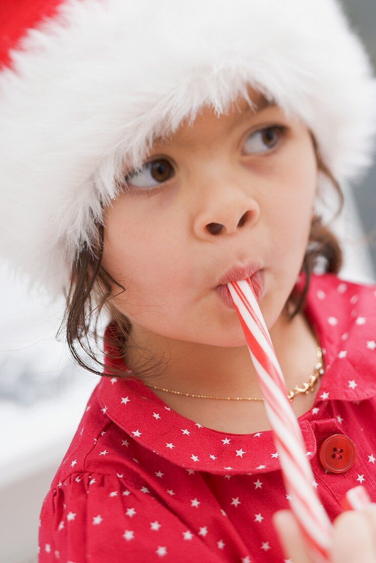 Small girl in Father Christmas hat eating candy cane