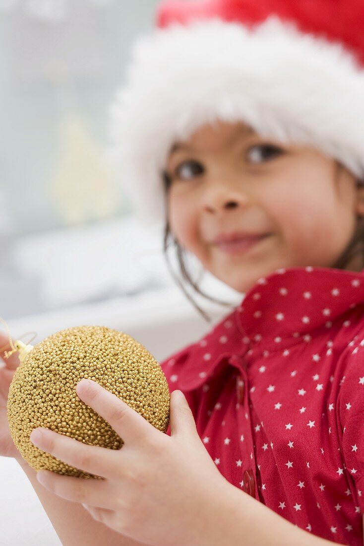 Small girl in Father Christmas hat holding Christmas bauble