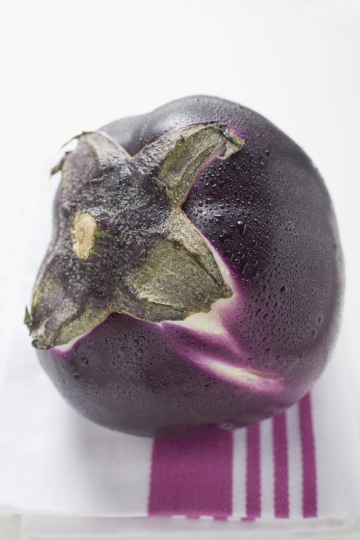 A round aubergine with drops of water on tea towel