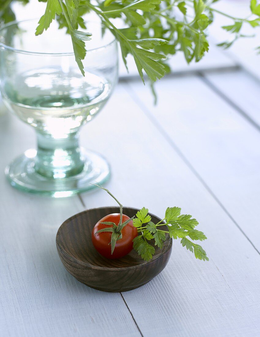 Tomate mit Petersilie im Holzschälchen und ein Wasserglas