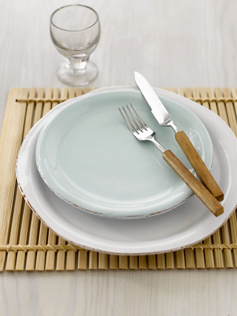 Place-setting with knife and fork on wooden mat, glass