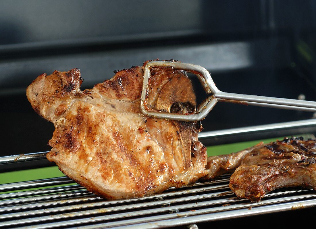 Turning pork chop with grill tongs