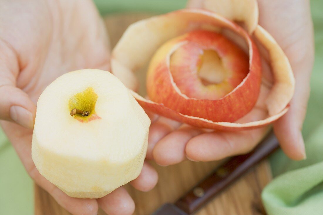 Hände halten einen geschälten Apfel und Apfelschale