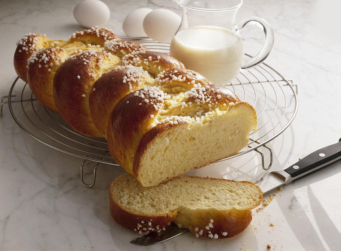 Bread plait with pearl sugar, milk jug & eggs in background