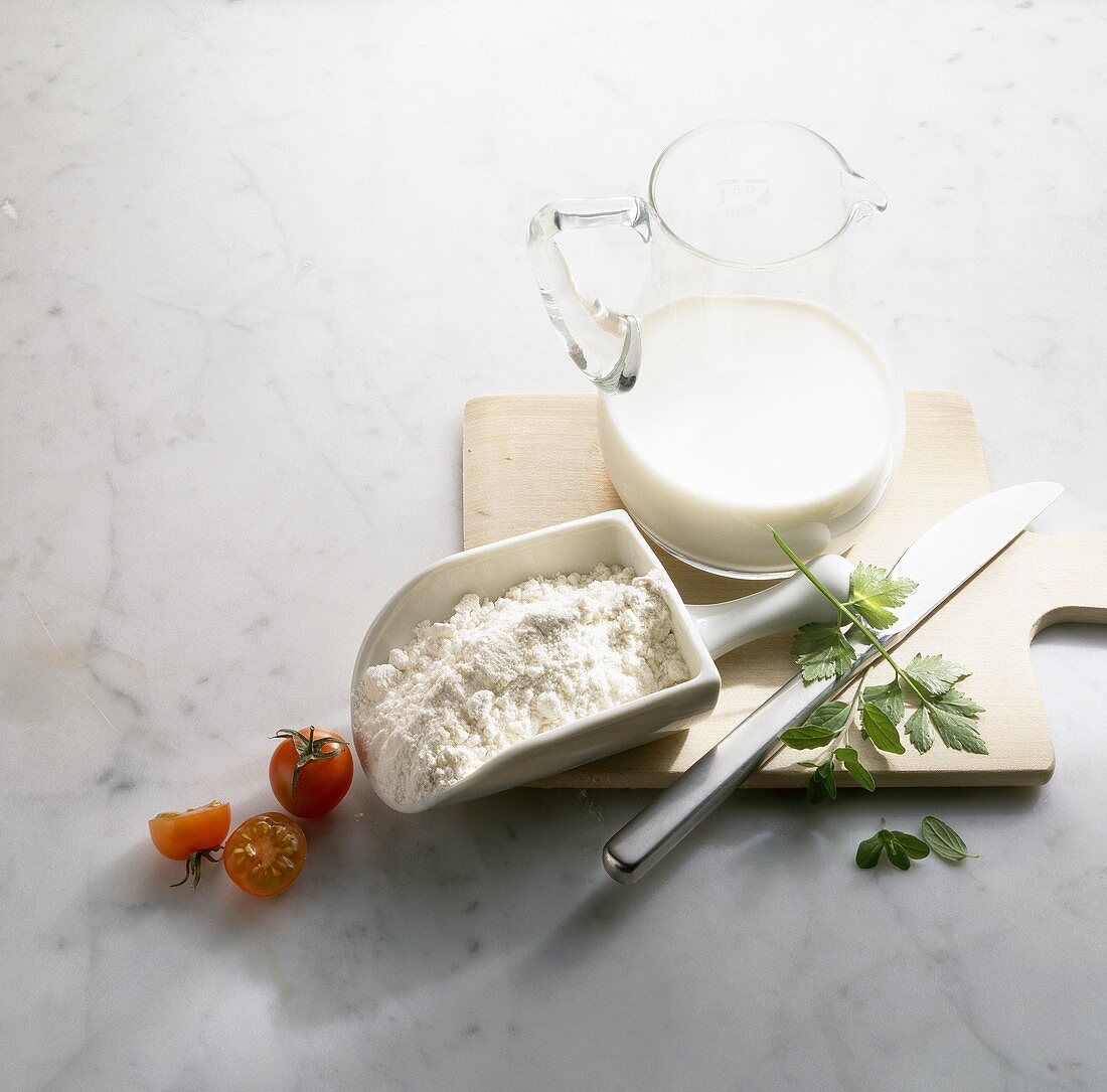 Jug of milk and scoop of flour on wooden board