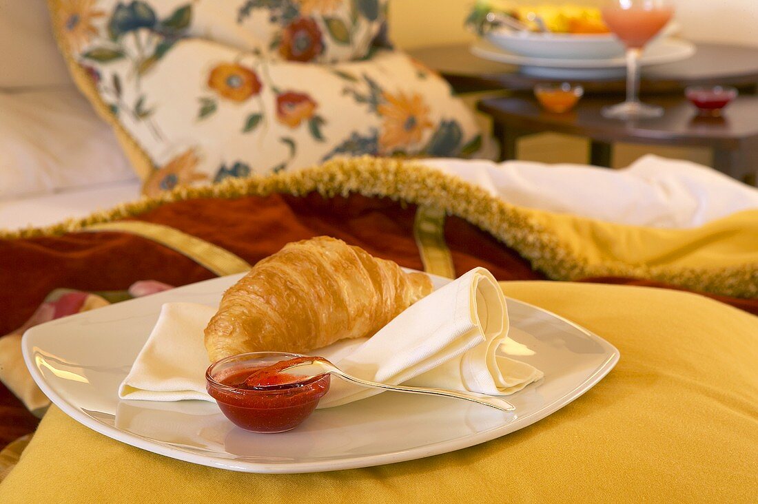 Teller mit Croissant und Marmelade auf einem Bett