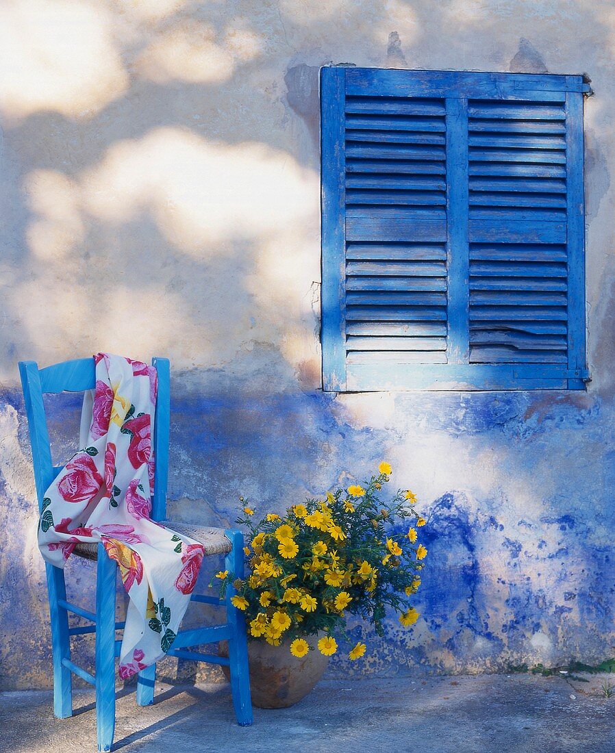 Gartenstuhl mit Tuch und Blumen an der Hauswand