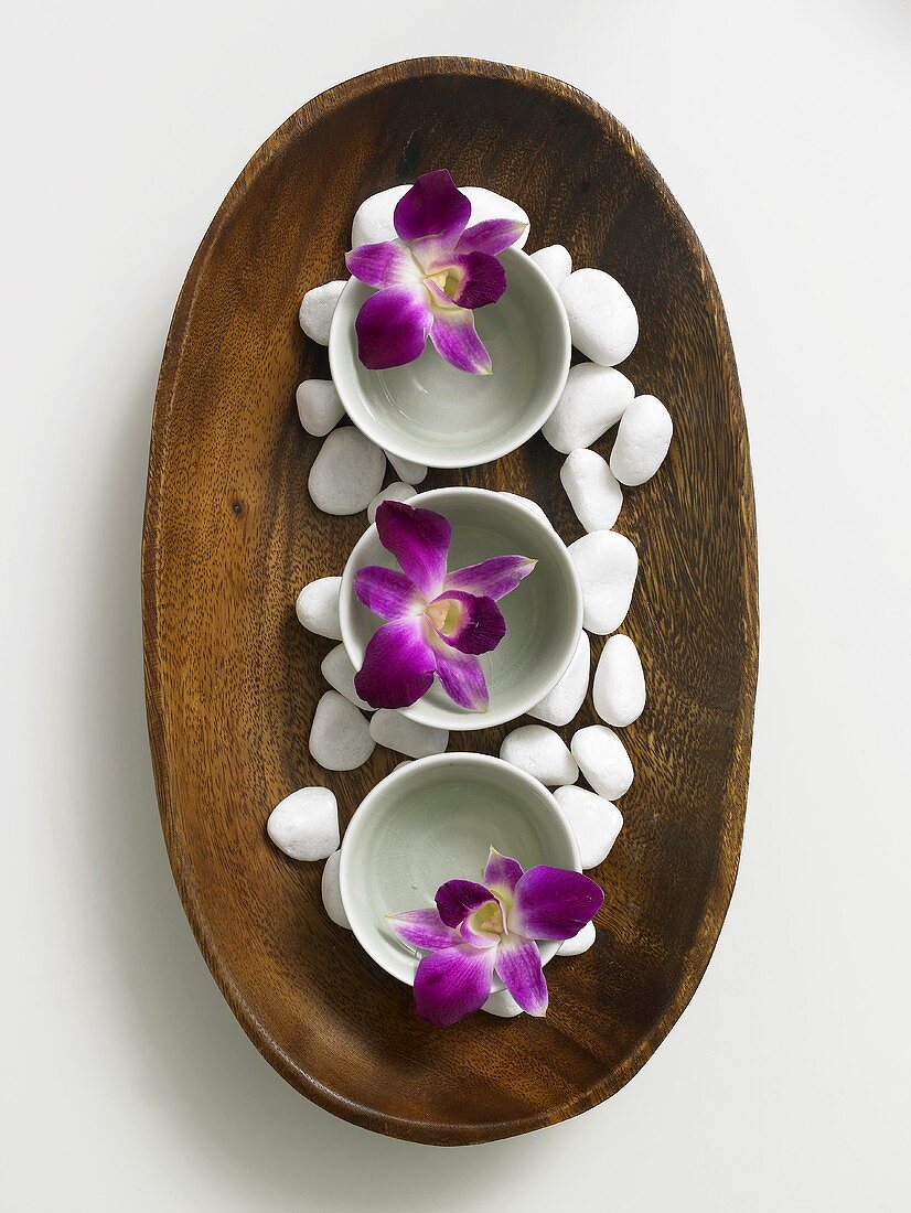 Flowers in small bowls and pebbles in wooden dish