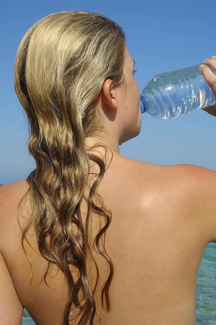 Frau trinkt Wasser aus einer Flasche am Meer