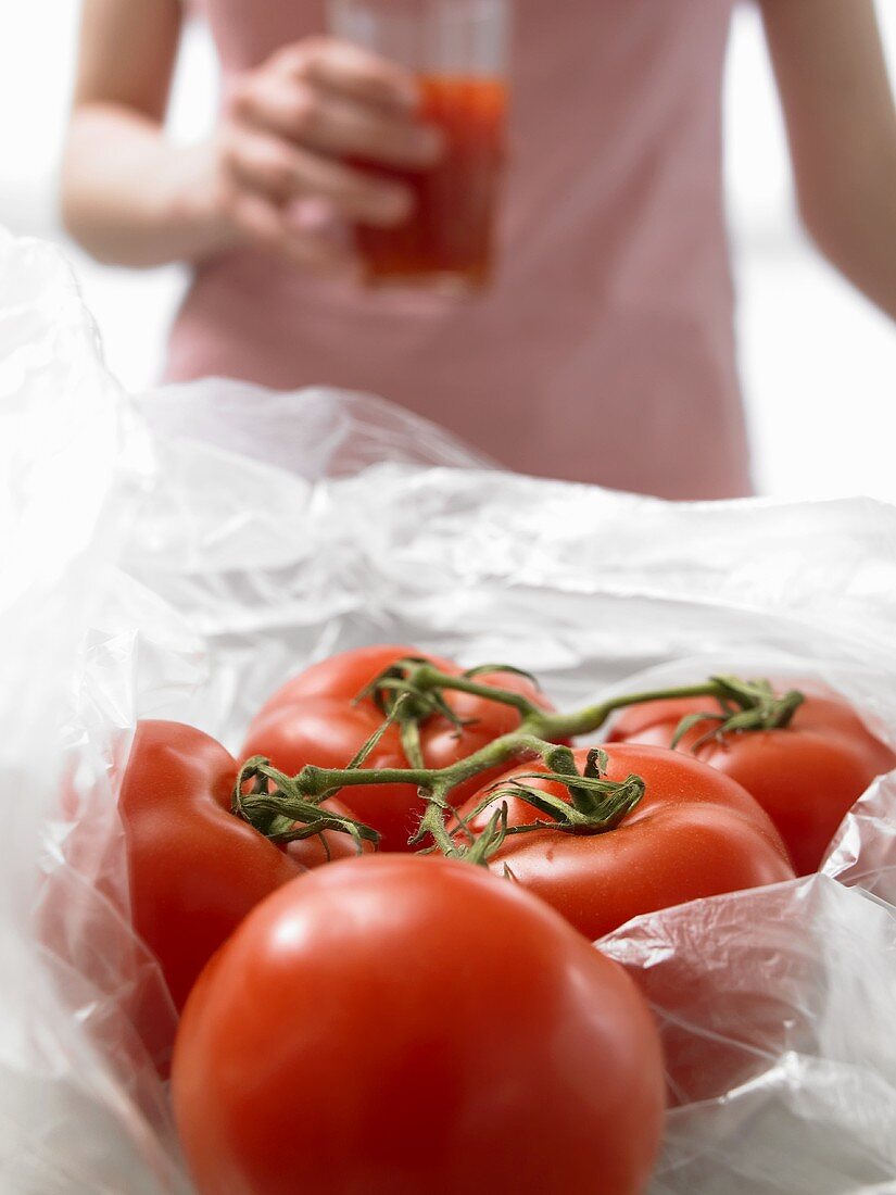 Tomatoes, woman with a glass of tomato juice in background