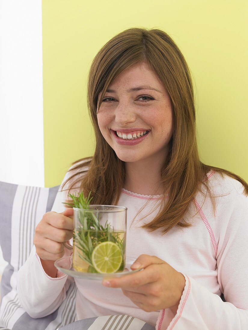 Junge Frau im Bett sitzend trinkt Tee mit Zitrone