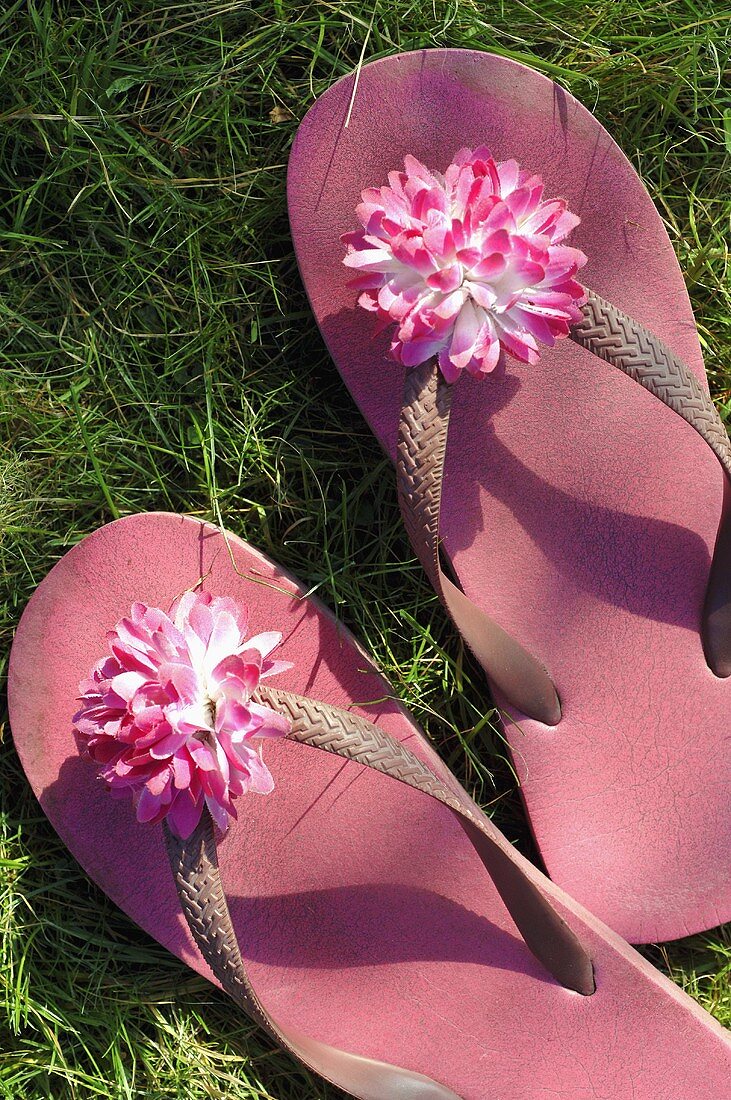 Rosa Flip-Flops mit Blüte im Gras