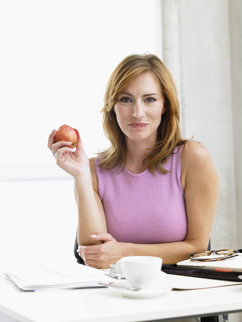 Frau sitzt am Schreibtisch und isst einen Apfel
