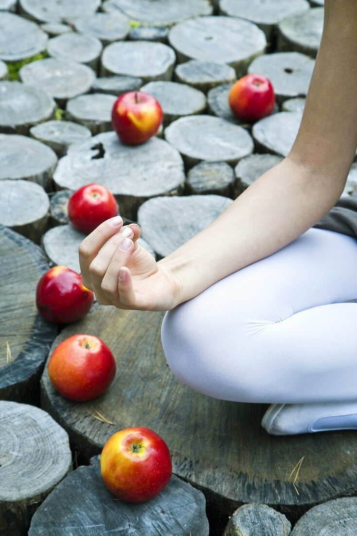 Young woman sitting on tree stump surrounded by apples