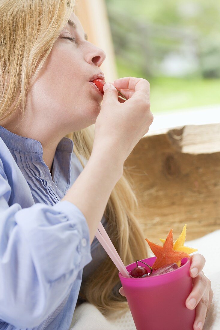 Blonde Frau isst die Früchte aus einem Fruchtcocktail