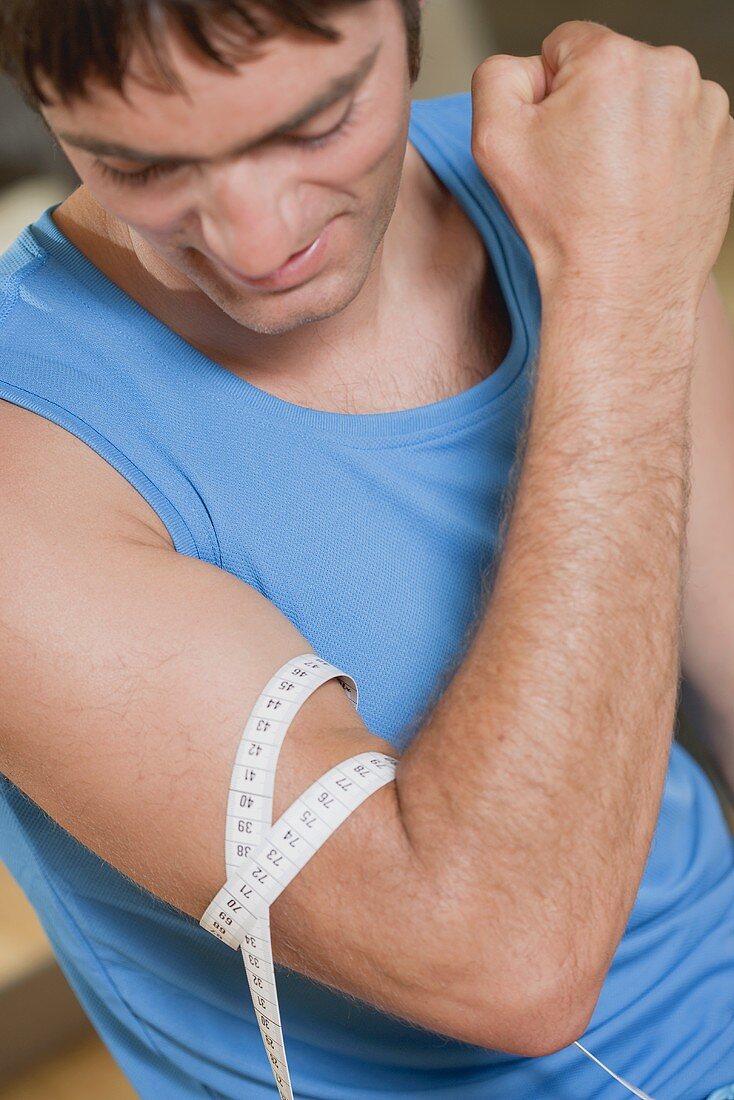 Young man measuring his muscle with a tape measure