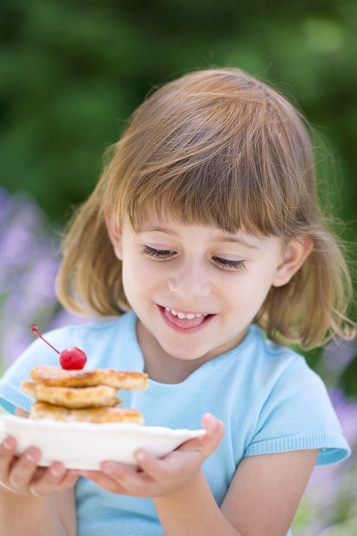 Kleines Mädchen hält Teller mit Apfel-Pancakes