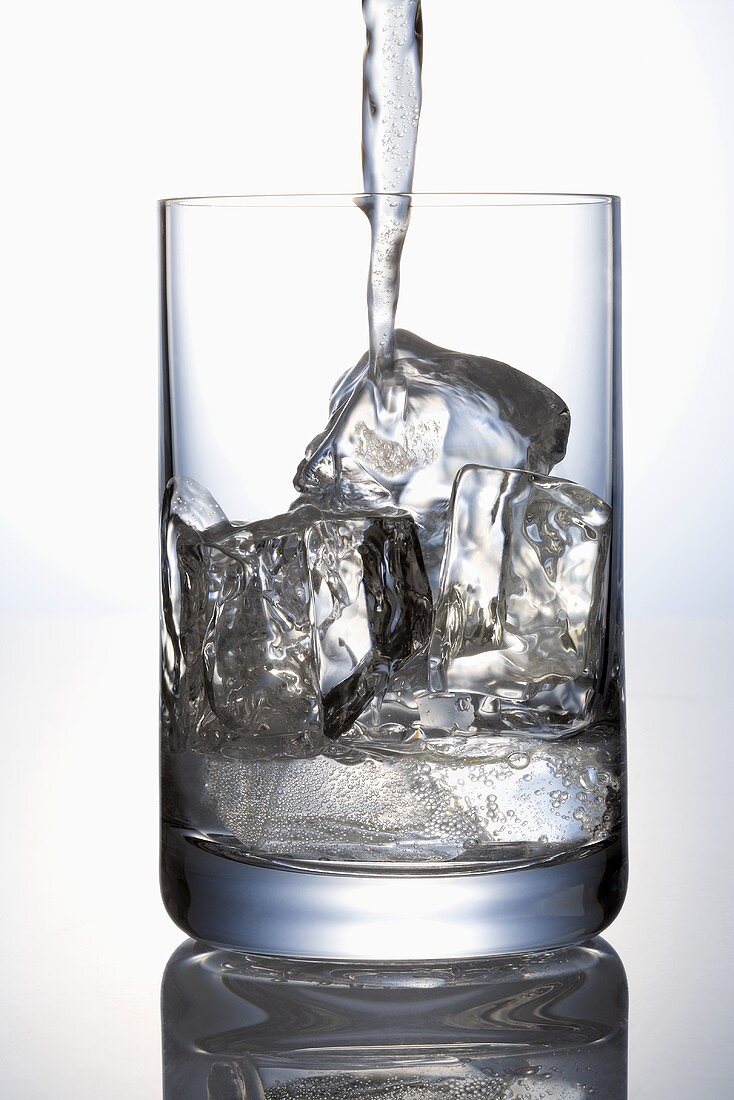Pouring water into a glass containing ice cubes