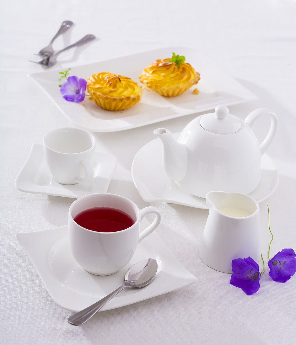 A cup of fruit tea, tea things and small cakes