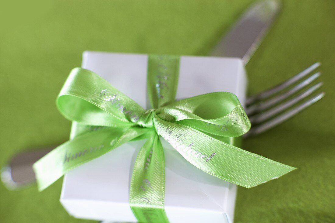 Kleines Geschenk mit grüner Schleife auf Gabel und Messer