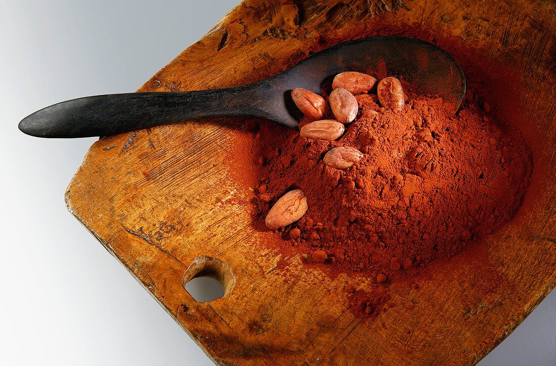 Kakaopulver und Kakaobohnen mit Löffel auf Holzbrett