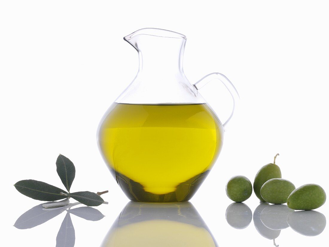 Olivenöl in Karaffe, grüne Oliven und Olivenblätter