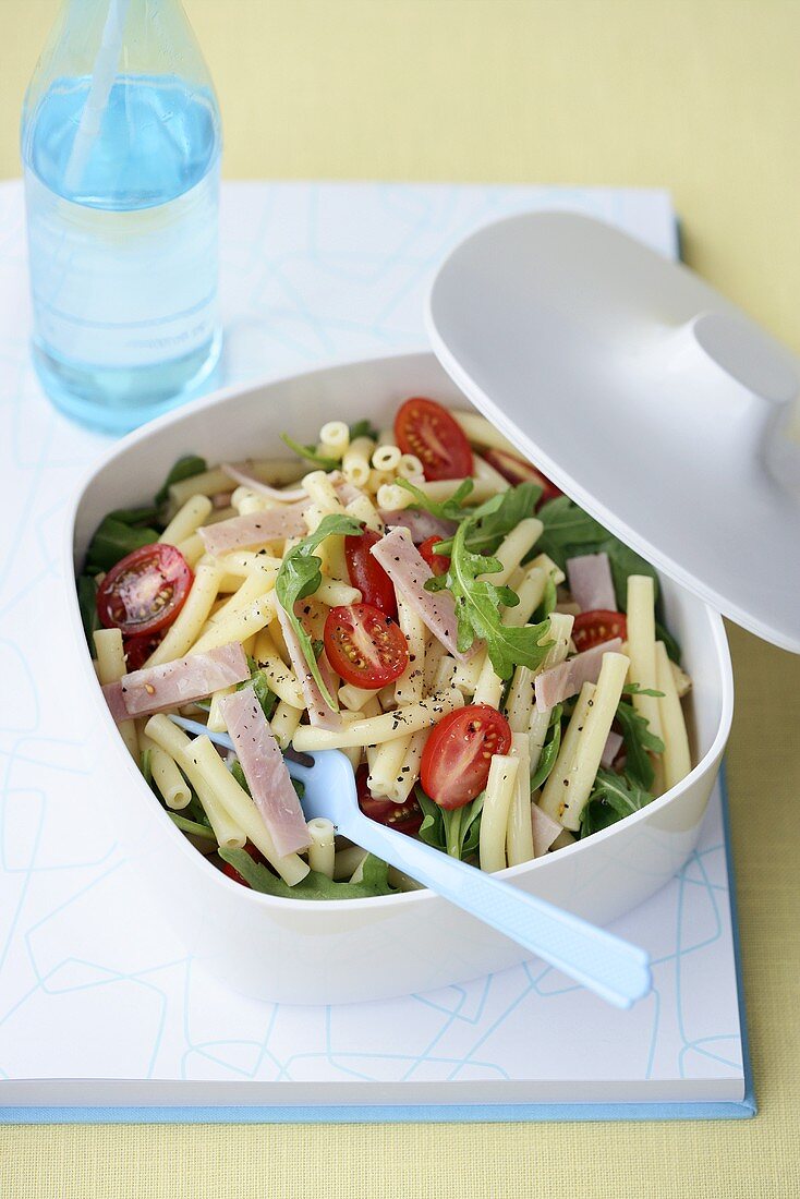 Pasta salad with ham, rocket and tomatoes in a plastic box