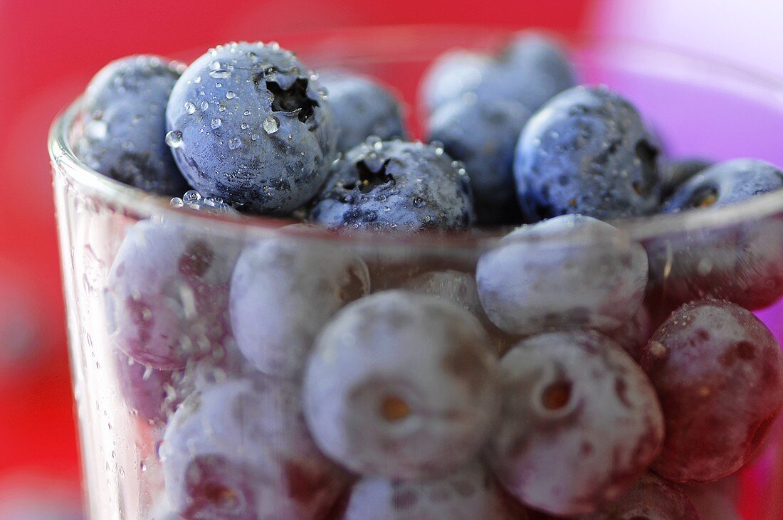 Viele Heidelbeeren mit Wassertropfen im Glas (Nahaufnahme)